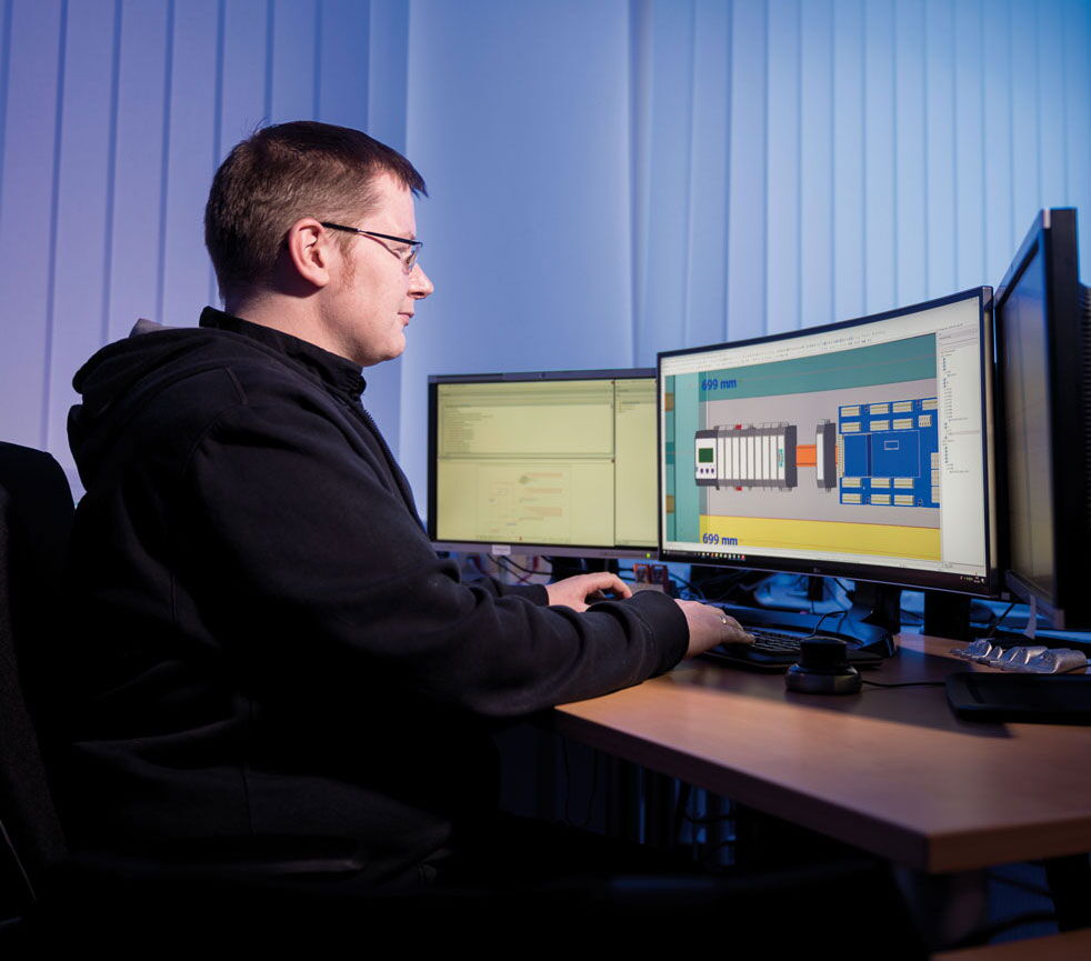 Mann sitzt vor 3 Computerdisplays